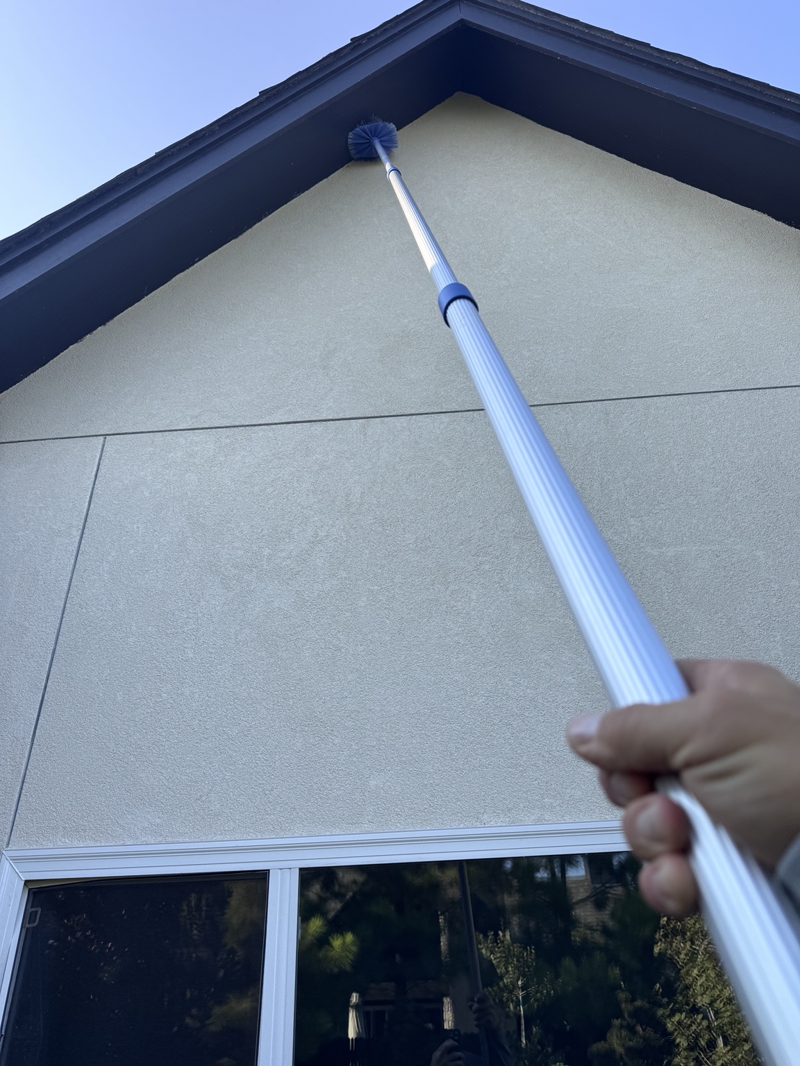 Long-reach brush removing cobwebs from a safely reachable exterior peak